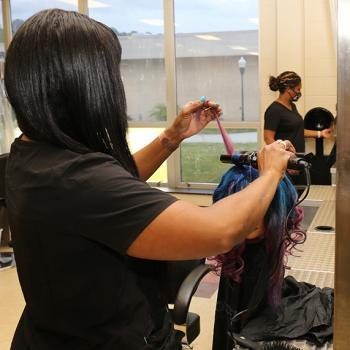 cosmetology student practices curling hair on wig