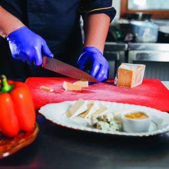 Chef in blue gloves slices cheese on red cutting board
