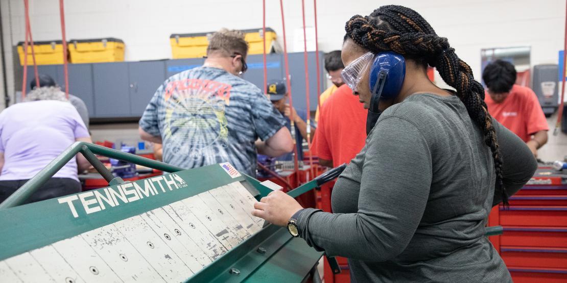 Woman in protective hearing muffs works on aircraft sheet metal