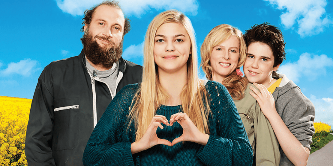 Teenaged girl with long blonde hair signs a heart while standing with her two parents and brother