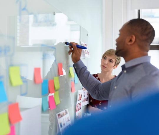 Three colleagues work together on business strategy while writing on whiteboard with colorful sticky notes