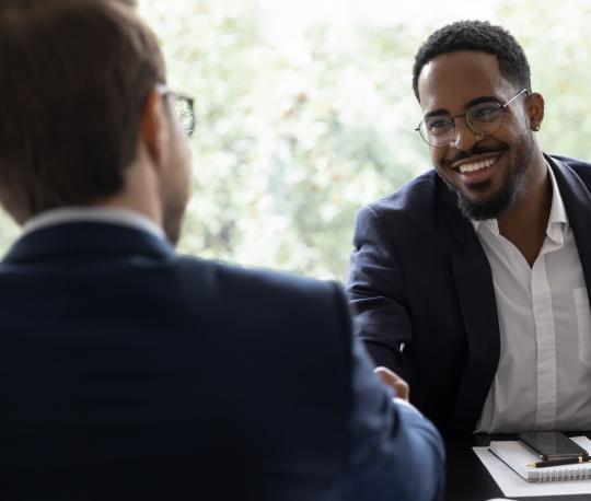 Man shakes his interviewer's hand while smiling woman looks on