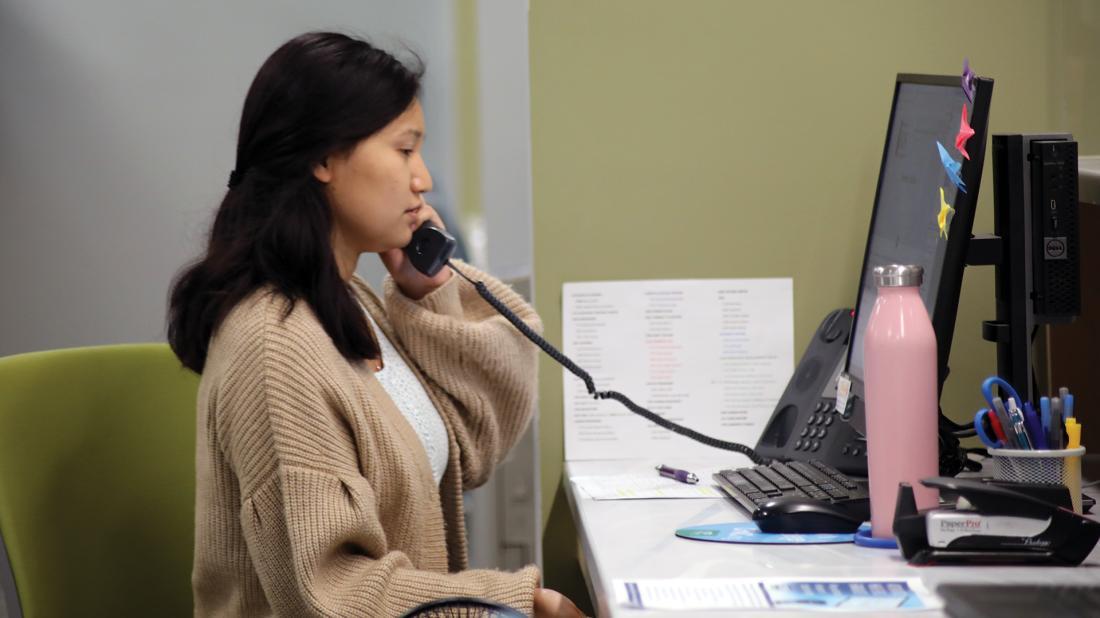 Federal work study student answers phone at a desk with computer