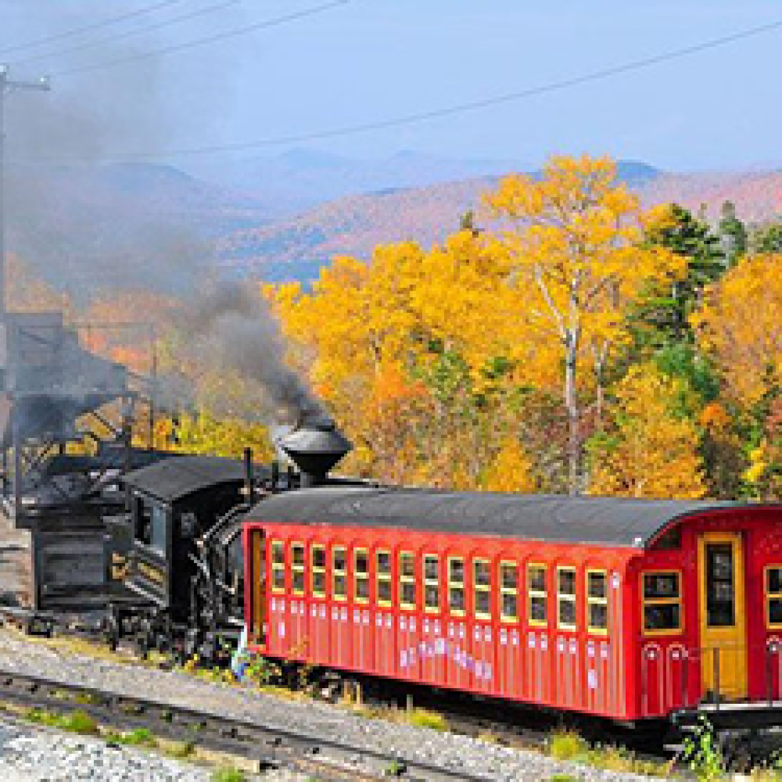 Black train car with red caboose traveling through mountainous countryside with trees changing to yellow during fall