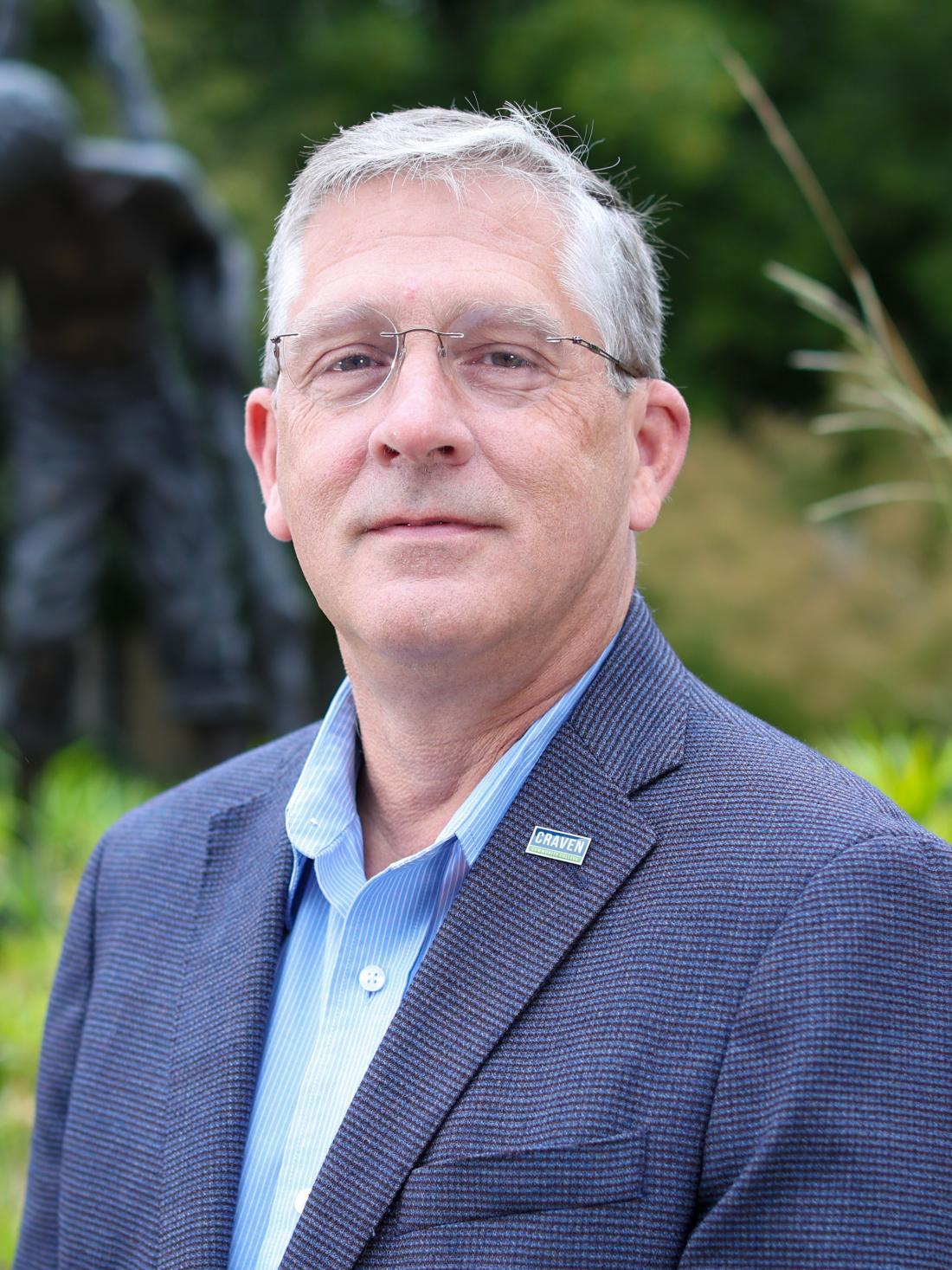 Craven CC President Dr. Ray Staats outside by Boy on Stilts statue