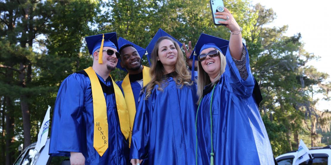 four graduates posing for a selfie outside